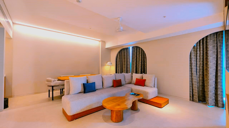 A bedroom and living area at Swosti Premium Beach Resorts, Puri, with a made bed, colorful seating, and an arched doorway.