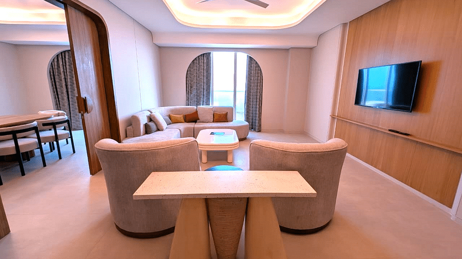 A living area at Swosti Premium Beach Resorts, Puri, with chairs, a table, and a view of a television.