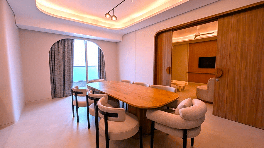 A dining area at Swosti Premium Beach Resorts, Puri, with a wooden table and chairs, and a view of the window.