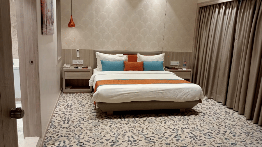 a contemporary hotel bedroom featuring a queen size bed, bedside tables, a ceiling-to-floor windows, and a door opening to the washroom at Lords Inn Rajkot