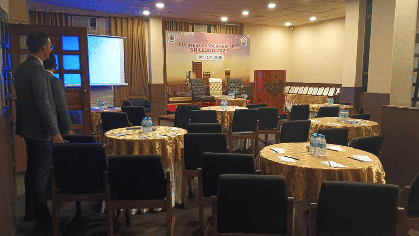 Indoor banquet hall set up for an event with round tables covered in golden cloths, cushioned chairs, and warm ceiling lights.
