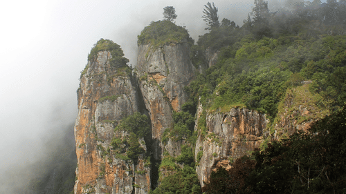 A far-out view of Pillar Rocks on a foggy day with vegetation around, a must-visit on a 2-Day Trip to Kodaikanal