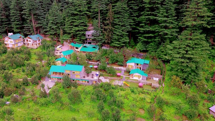 Aerial view of Amara Hotels and Resorts nestled in lush greenery, surrounded by dense pine forests with multiple buildings featuring green rooftops.