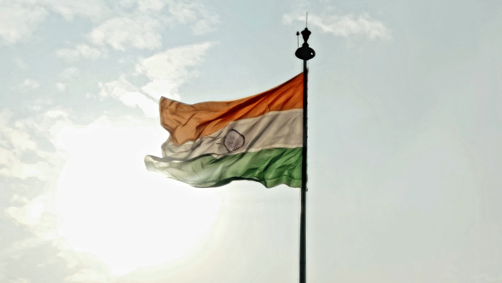 Indian tricolour flag fluttering against the bright sky with sunlight in the background, capturing the pride and patriotic spirit of India's Independence Day.