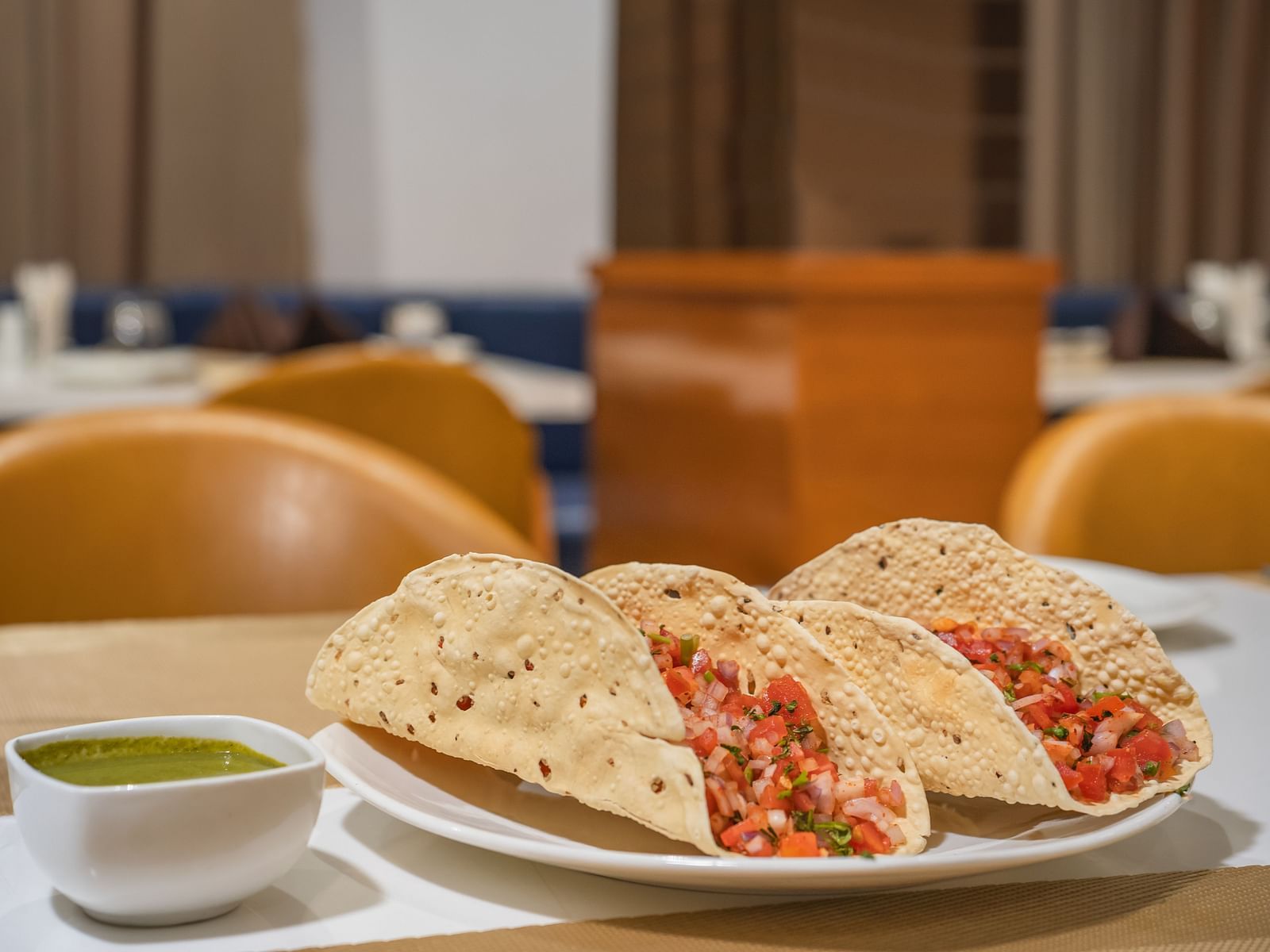 Three crispy shells filled with a vibrant mixture are served on a plate with a small bowl of green sauce