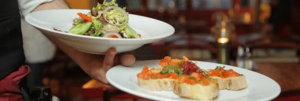 Image of a hand holding two plates of neatly plated food.