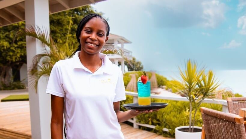 A woman in a white polo shirt and black pants stands on a wooden deck outdoors.