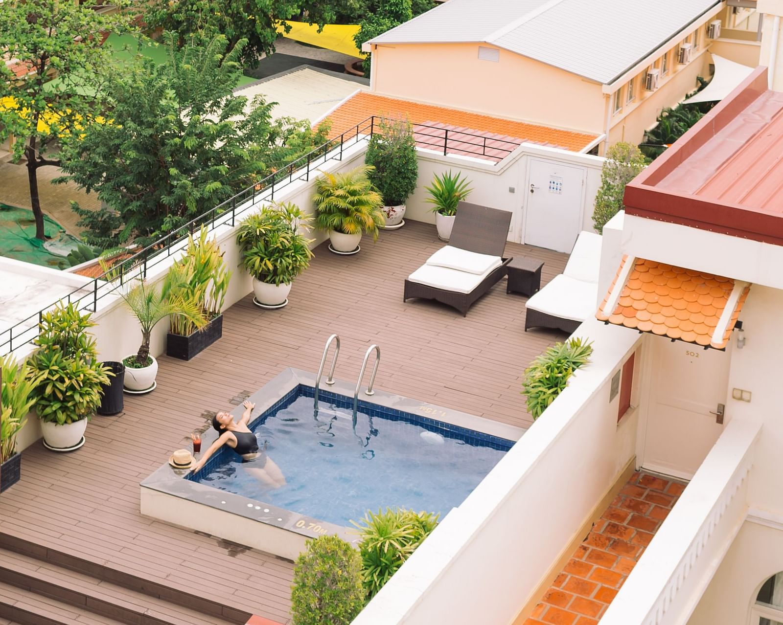 An aerial view shows multiple buildings with orange-tiled roofs and a swimming pool surrounded by trees and greenery | Central Mansions, Phnom Penh