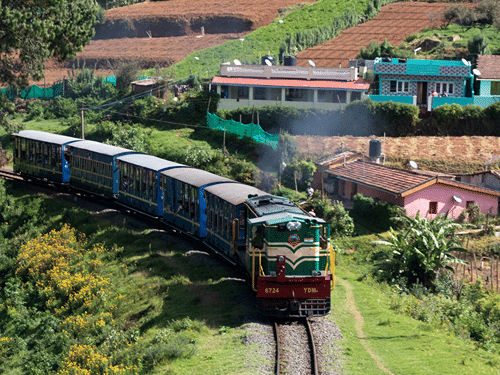 An aerial view of the toy train (Ooty) travelling on the tracks with buildings in the background.