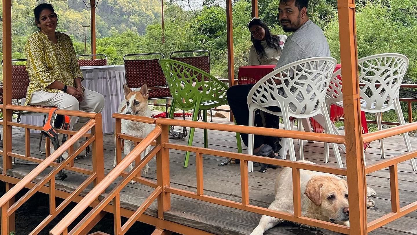 Three people sitting on a shared bench with a dog at The Sylvan Retreat, Dehradun.