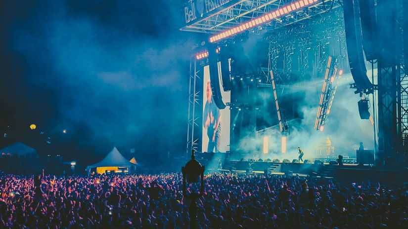 Open-air concert stage lit up at night with a cheering crowd in front.