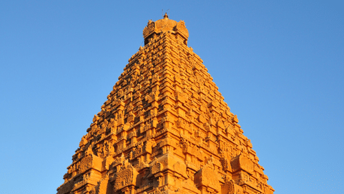A far-out view of a Shiva Temple with the sun shining on the outer wall and blue sky in the background.