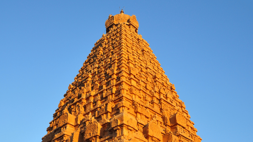 A far-out view of a Shiva Temple with the sun shining on the outer wall and blue sky in the background.
