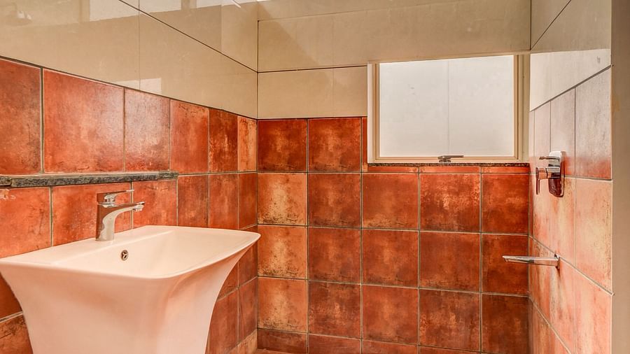 A spacious washroom at Harigovinda's JNStay, with a washbasin to the side and a shower head at the furthest end