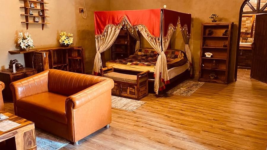 An image of a bedroom with poster bed decorated with fabric pieces, and there is also a seating area consisting of sofa and a table - Themis Mudhouse - An Ethnic Resort & Cultural Dining
