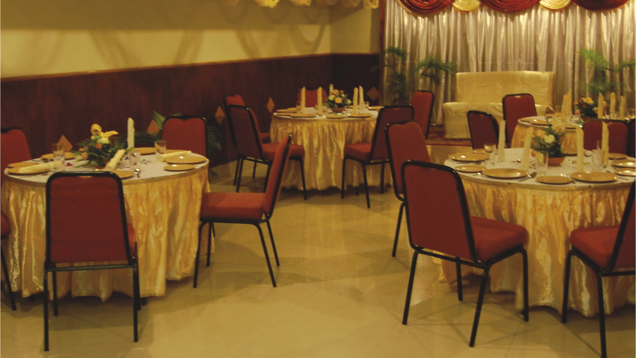 A decorated wedding banquet hall with round dining tables, gold table linens, and red chairs - Hotel Pandian