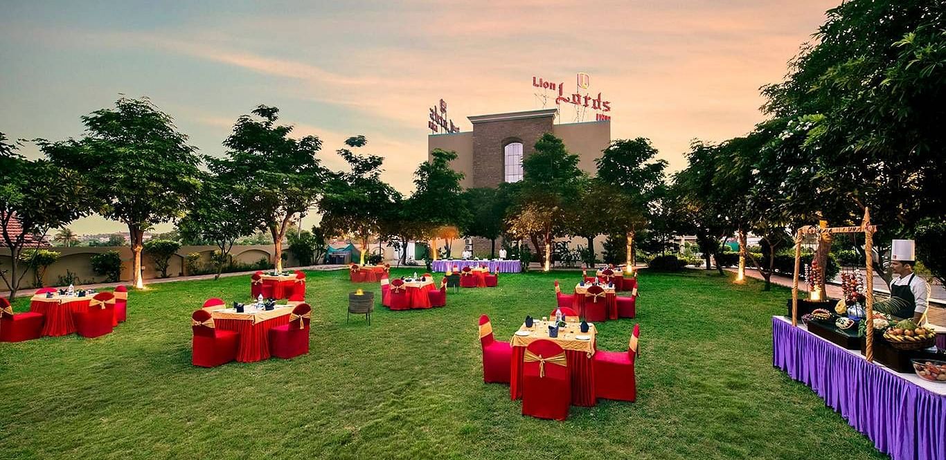 An outdoor area is prepared for an event with tables covered in red cloths on the grass - Lion Lords Inn Rajula