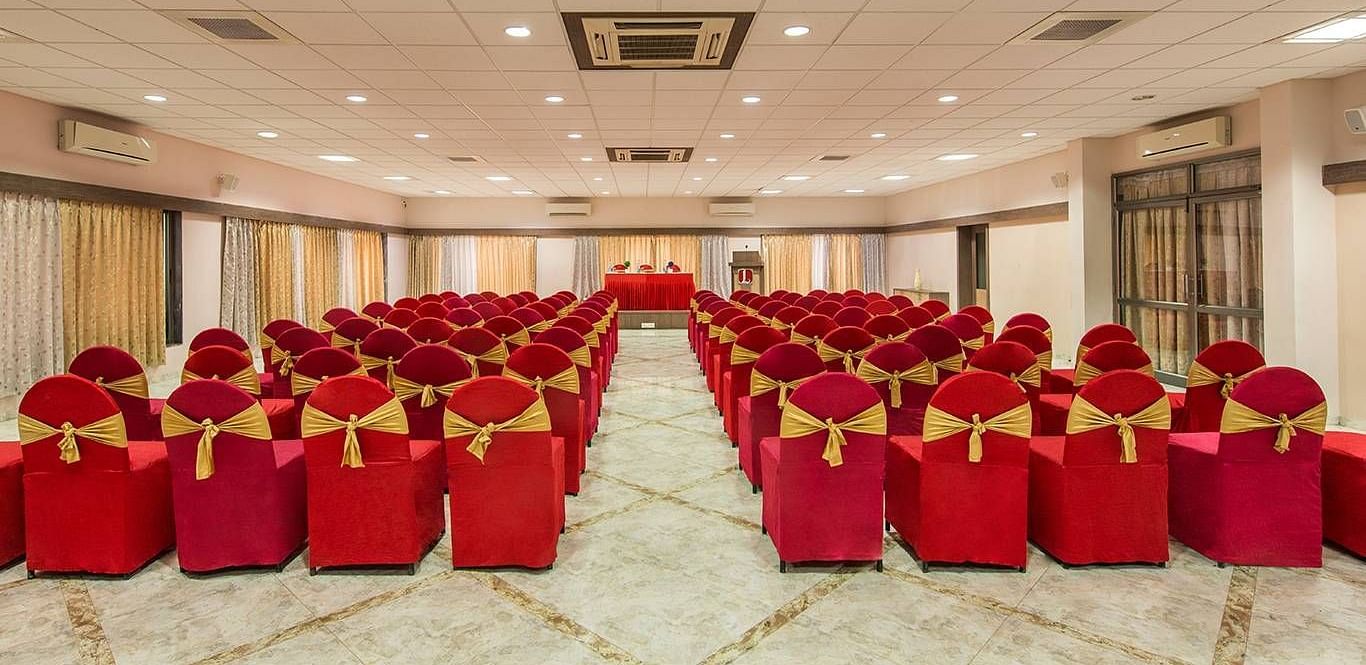 A large hall is set up with rows of chairs covered in red fabric for an event - Lion Lords Inn Rajula