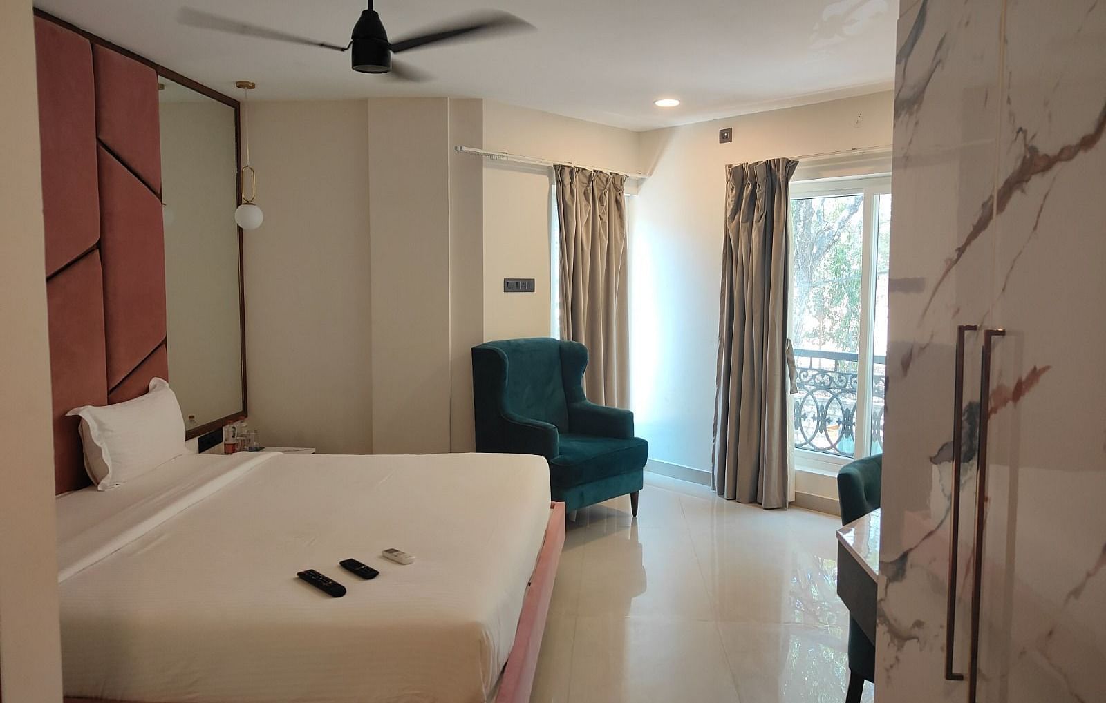 a plush double bed and a teal coloured cushioned arm chair at the junior suite - Astra Hotels and Suites, Koramangala