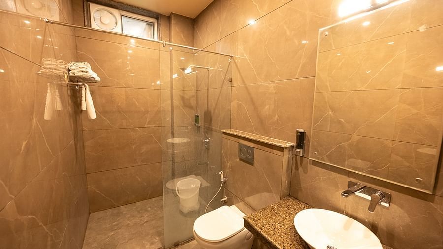 A modern bathroom of Oak Room with marble-effect tiles features a glass shower enclosure, toilet, and a vanity with a counter-top basin at The Pavilion, Nainital
