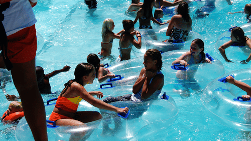 A crowded swimming pool with people relaxing on inflatable floats and enjoying the water on a sunny day.
