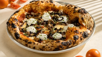 thick-crust pizza topped with burrata cheese, olives, and herbs, served on a white plate with apricots in the foreground and background at Gemini Continental