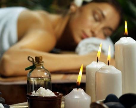  A person lying on a massage table in a spa setting, with lit candles and various spa products nearby.
