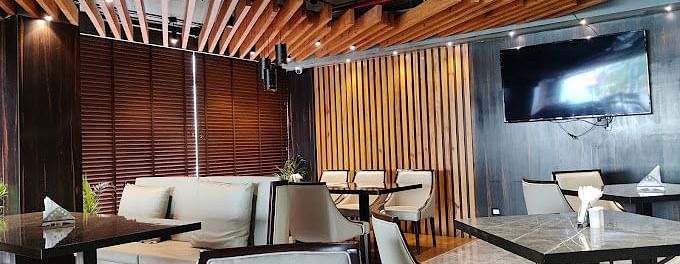 A restaurant with modern tables for four, wooden decorations towards the wall and ceiling, along with a wall-mounted TV at Yashshree The Imperial Inn, Siliguri.