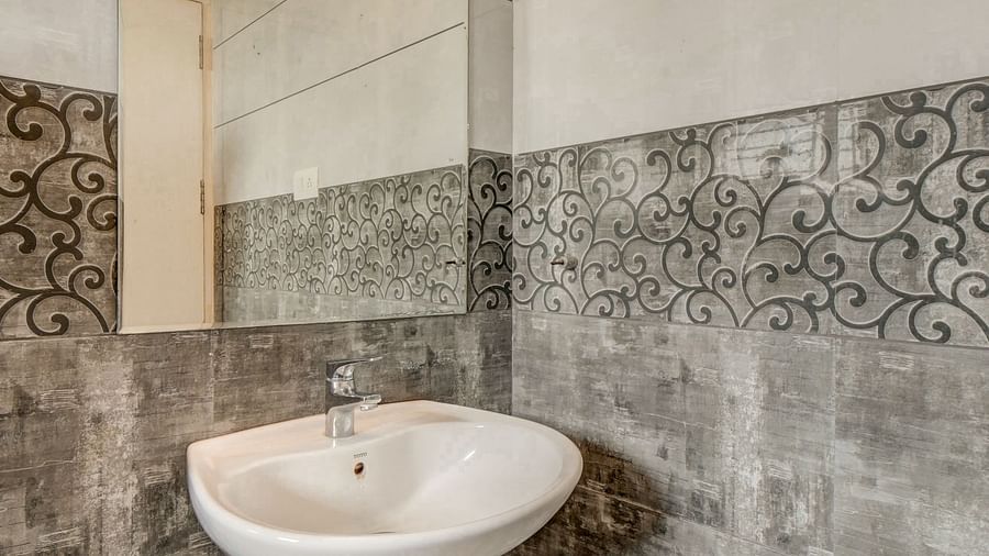 A spacious washroom at Harigovinda's JNStay with a wall-mounted mirror, washbasin below it, and bright lighting