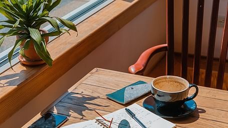 A cup of coffee a diary glasses and mobile phones on a table at a cafe