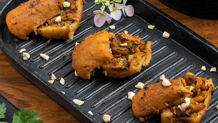 A delicious dish served on a grilled plate, garnished with sesame seeds, finely chopped onions, and a sprig of coriander.