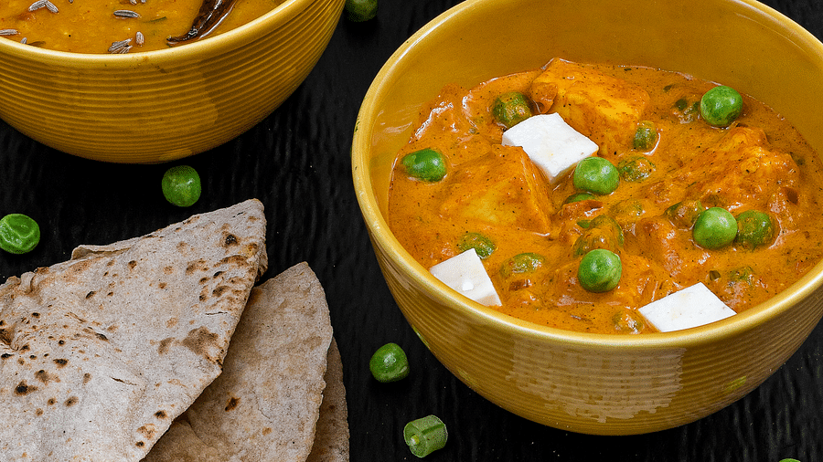A variety of Indian dishes served in bowls, including rice, flatbread, dal, matar paneer, and assorted vegetables.