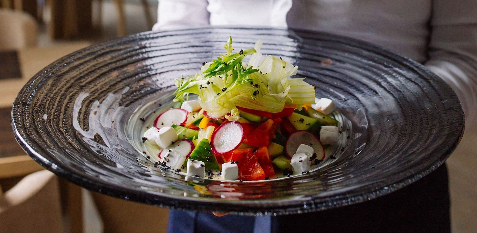 A waiter holding a beautifully plated dish wih fresh salad in a restaurant -  Sitara Luxury Hotel in Hyderabad near Ramoji Film City.