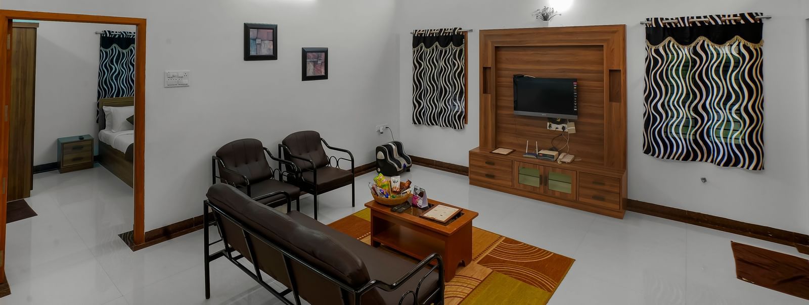 Living room with a sofa and wall-mounted television with a wooden cupboard at WOW Bungalow, Yercaud.