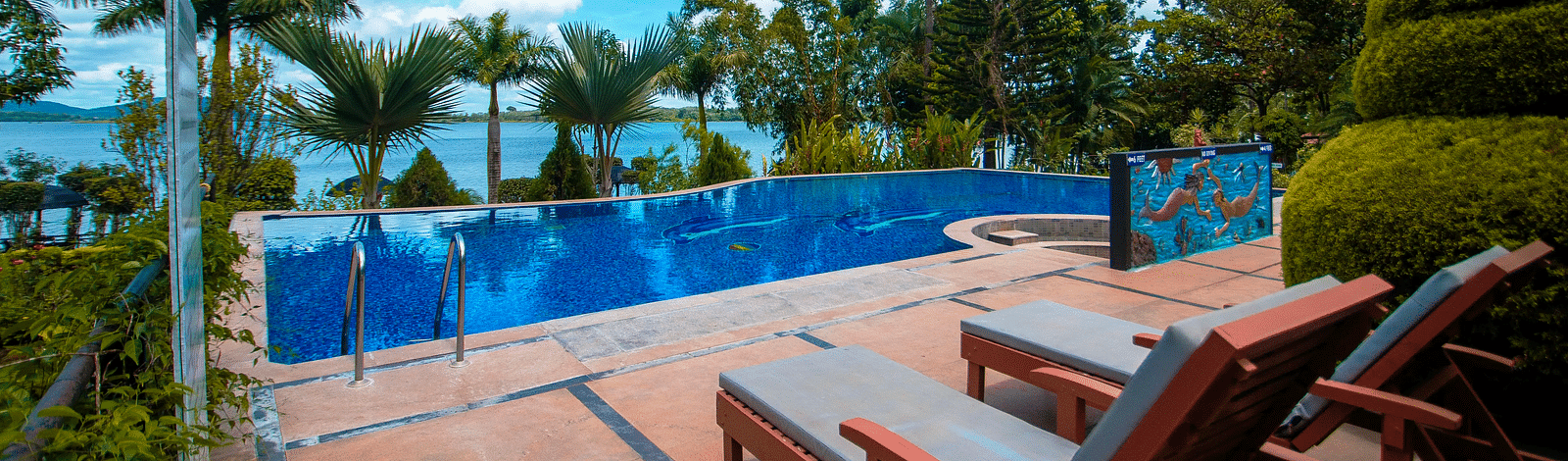 A swimming pool with sun loungers on the side at Coorg Jungle Camp Backwater Resort, Kushalnagar.