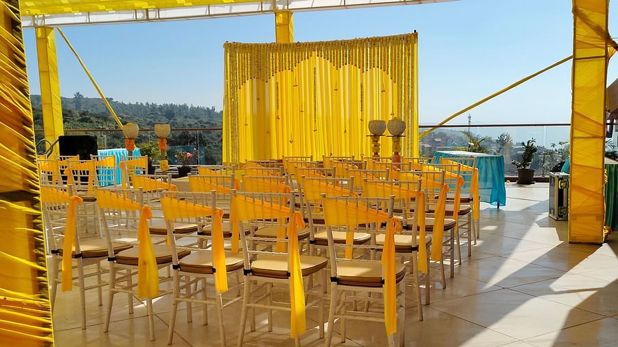 A courtyard where several chairs with yellow fabrics are set up near a stage which is also decorated by yellow fabrics and  flowers  where people are going to gather for pre wedding functions at The Grand Legacy Resort & Spa