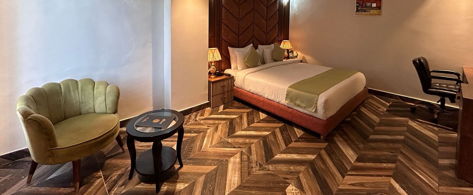 Image of Super Deluxe Room at DLS Grand Luxotica, Dehradun featuring a sitting space including a couch and a coffee table placed at a distance from the plush bed under warm lighting