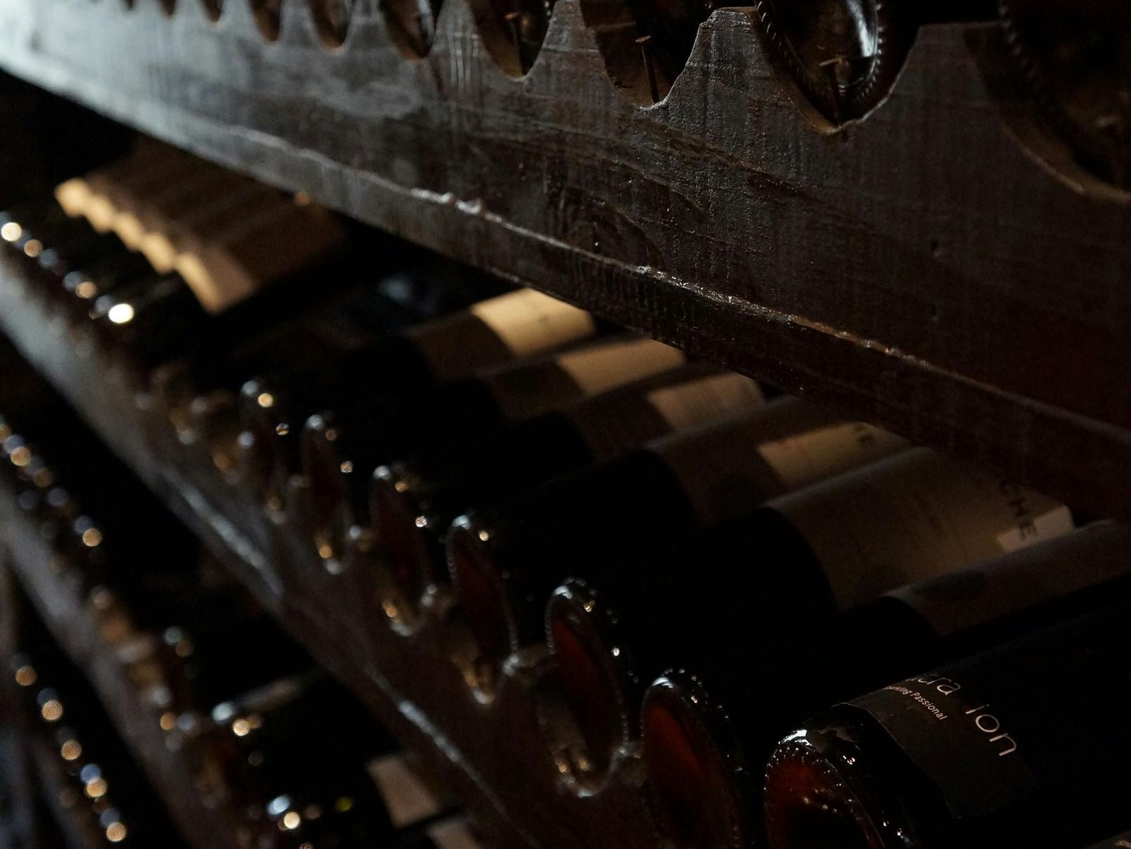 Rows of wine bottles resting in a dimly lit cellar, showcasing an elegant and aged wine collection.