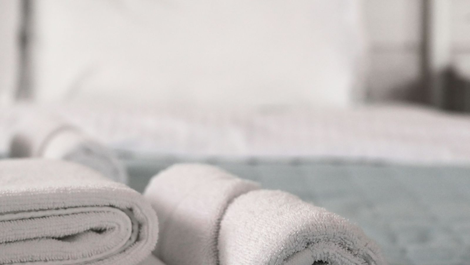 A close-up of neatly folded and rolled white towels on a bed with a blurred headboard