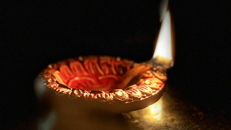 A close up of a lit diya used for many celebrations, including Karthigai Deepam, with the background blurred.