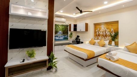 A hotel bedroom featuring twin beds with yellow runners, a wall-mounted TV, and wall decor | Hotel Aurora Bliss, Gachibowli