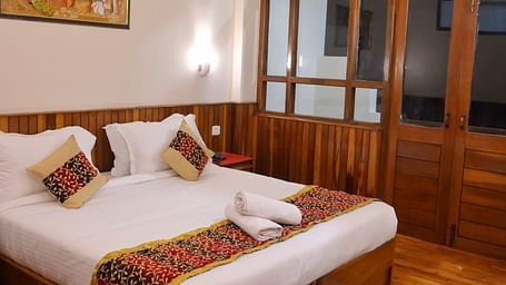 An image of the super deluxe room featuring a queen size bed, bed side table, lamps, and an expansive door leading to the balcony - Sumitel Chiminda, Pelling