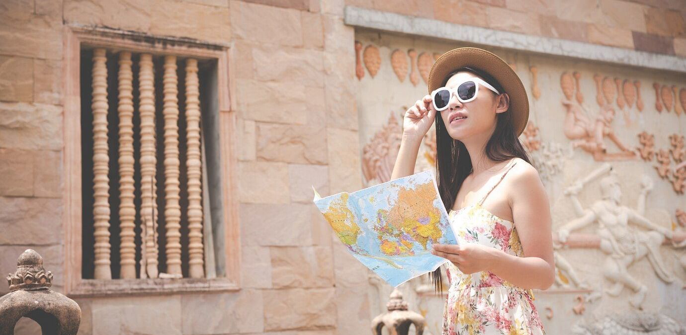 A person holding a map while standing in front of a building with stone walls and a decorative window.