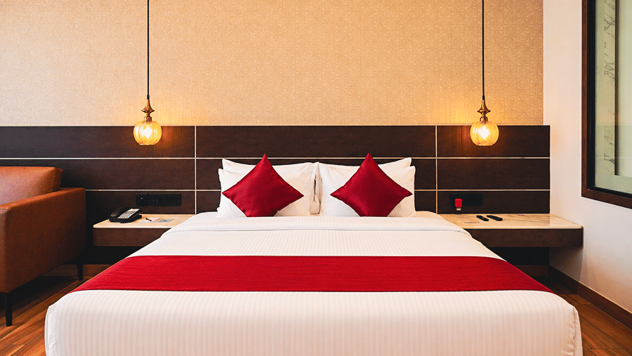 Spacious king-bedded guest room with warm lighting, wooden flooring and modern interiors at HM Hotel & Resort, Dibrugarh, offering a comfortable stay in Assam