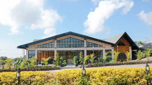The Mausmai Ballroom features a grid-patterned glass facade, flooding the space with natural light and offering panoramic views of the lush garden outside.