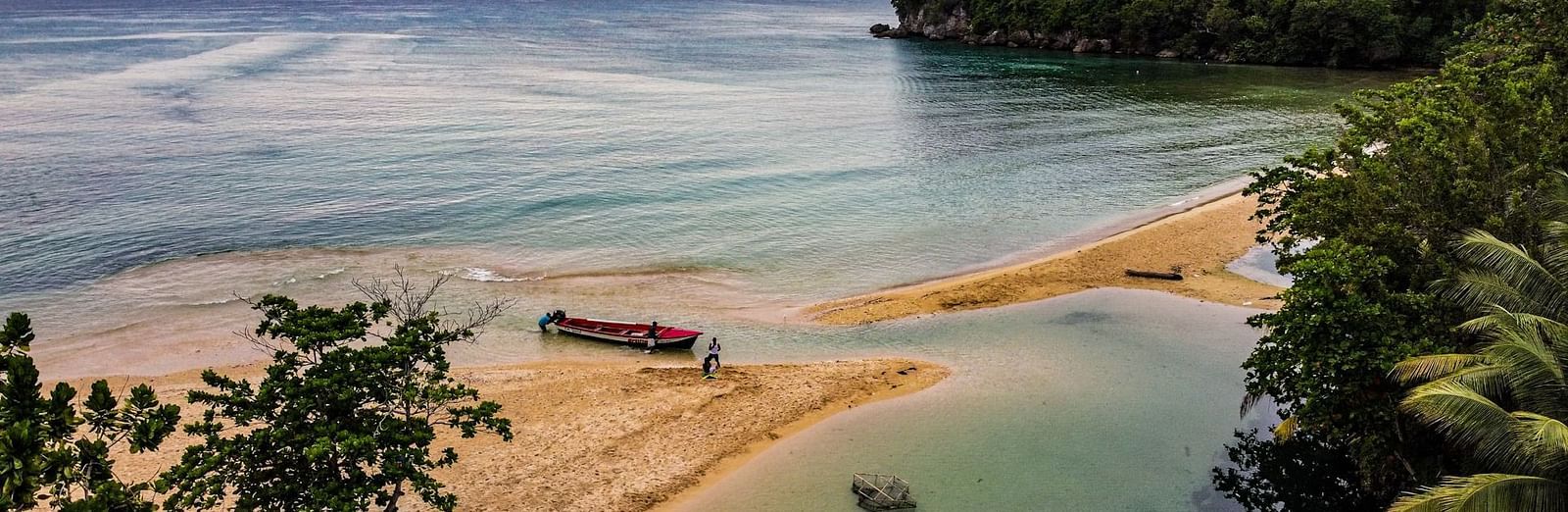 An aerial view of a secluded beach where a narrow strip of sand meets the water, surrounded by lush greenery.