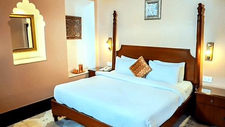 A room with a large bed, spreads, pillows, and lights. | Hotel Devnadi, Haridwar