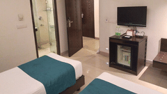 A room with twin beds, a wall-mounted TV, minibar, and open bathroom door at Rockland Hotel, Panchsheel Enclave, New Delhi.