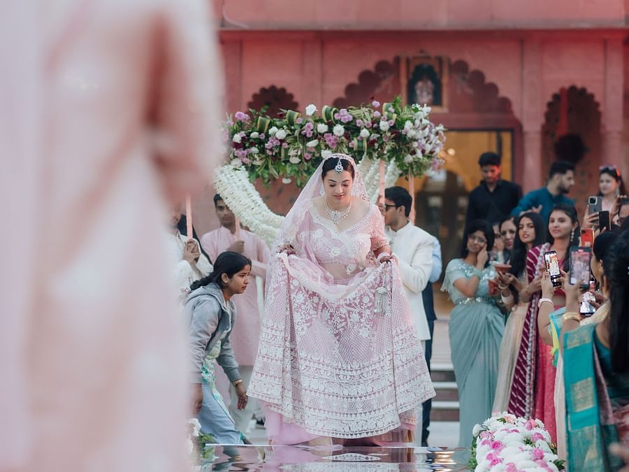 Bride and groom walking down a flower-lined aisle with a red heritage-style building in the background.