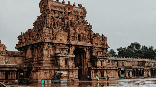 image of a temple constructed in dravidian architecture with a wet foreground and a cloudy sky in the background